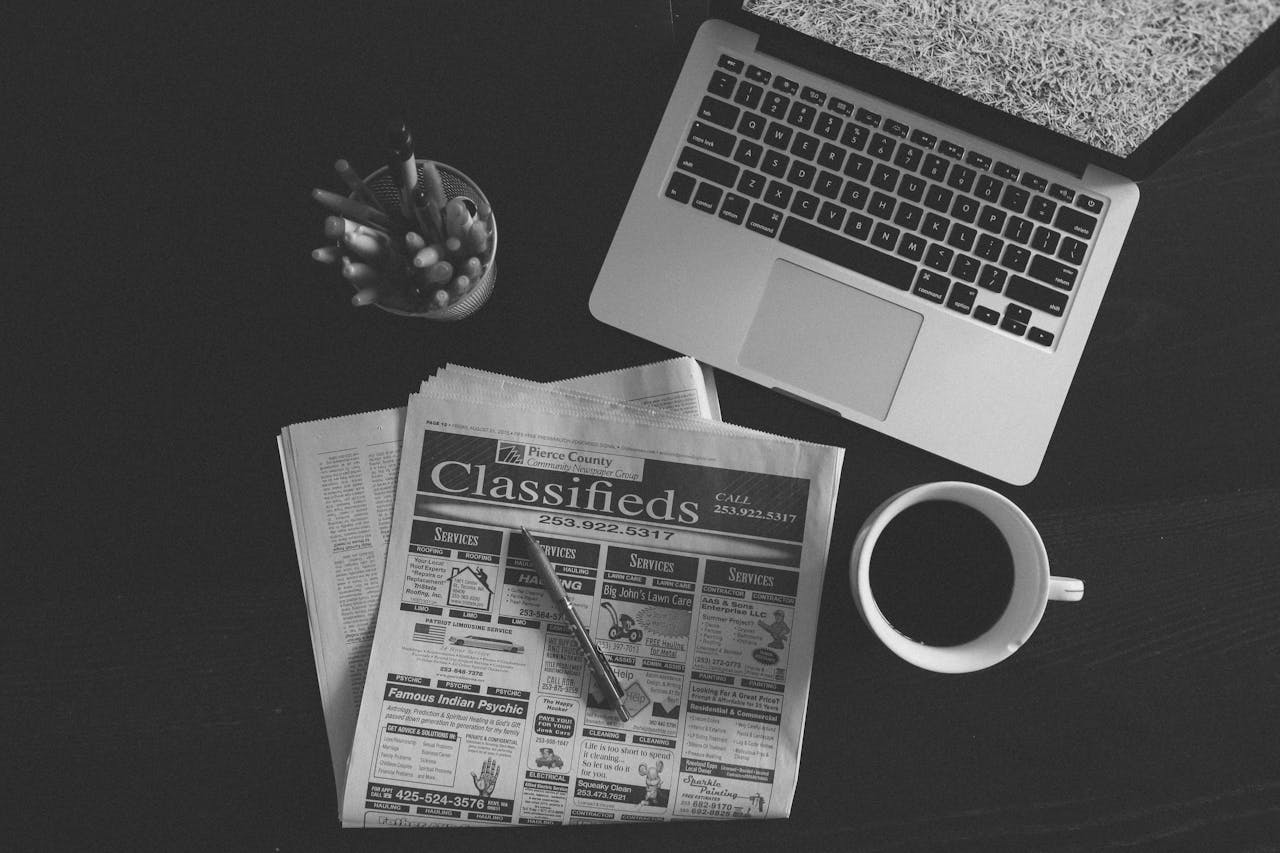 get-in-touch A black and white image of a laptop, newspaper, and coffee cup on a desk.