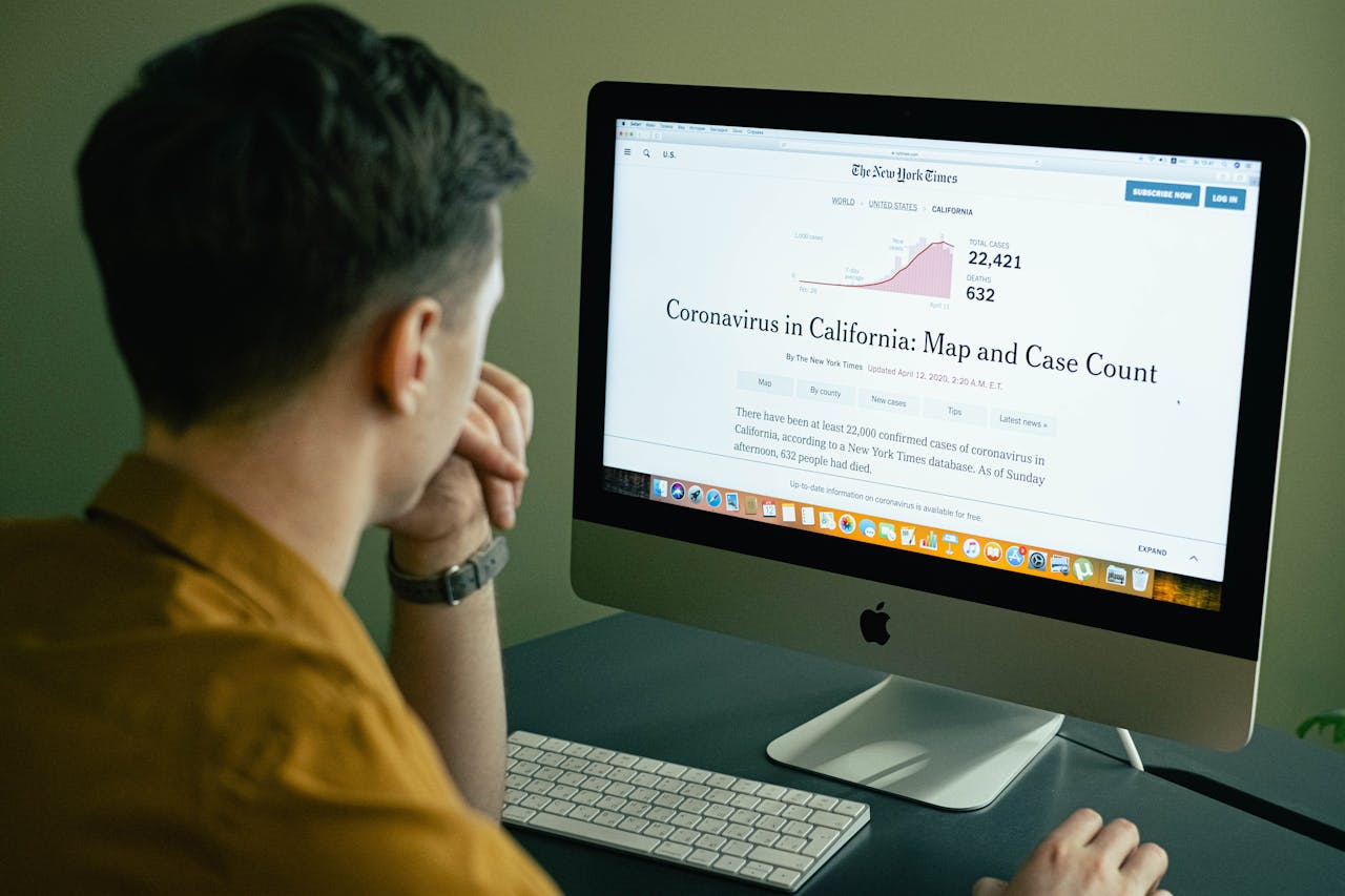 services-01 A man reading a coronavirus case count article on a computer screen indoors.